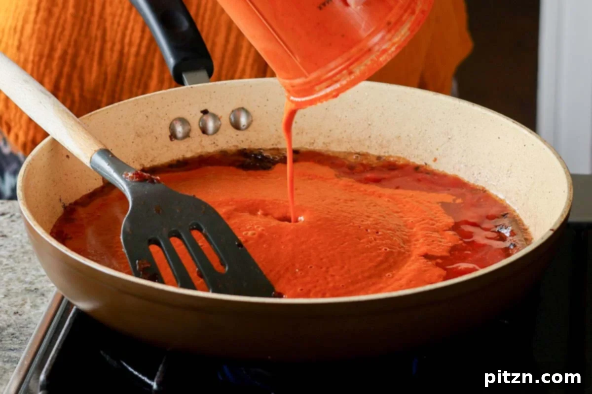 The vibrant blended tomato and chili sauce being poured into the skillet with tempered whole spices