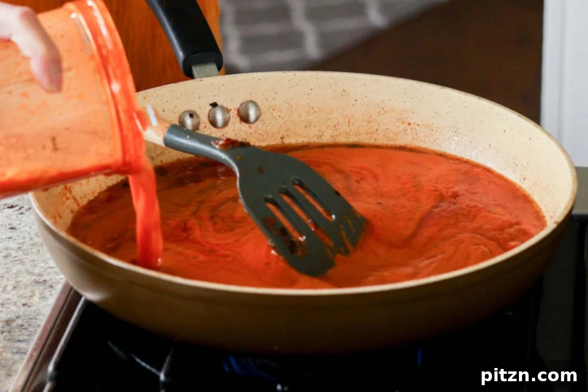 Pouring water from rinsing the blender into the skillet with the sauce
