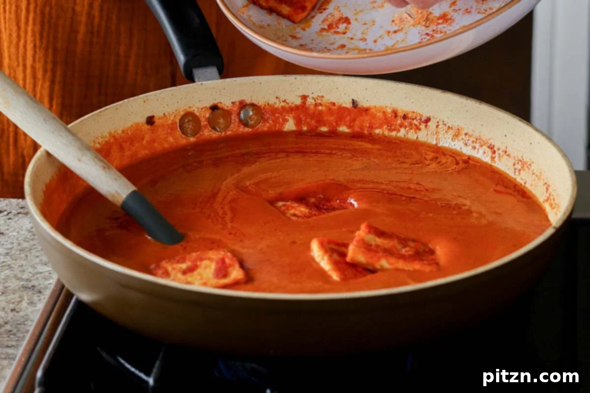 Crispy, golden-brown tofu pieces being added into the rich red curry sauce in the skillet