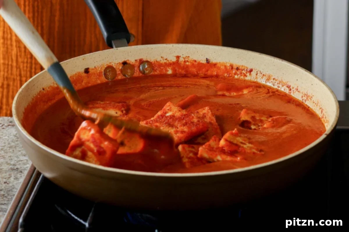 Tossing the crispy tofu gently into the simmering red curry sauce to coat evenly