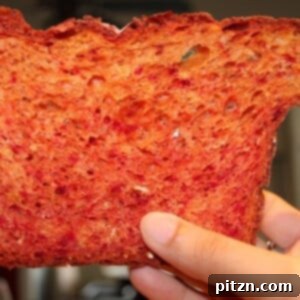 A vibrant slice of beetroot bread with orange zest being held up, showcasing its beautiful color.