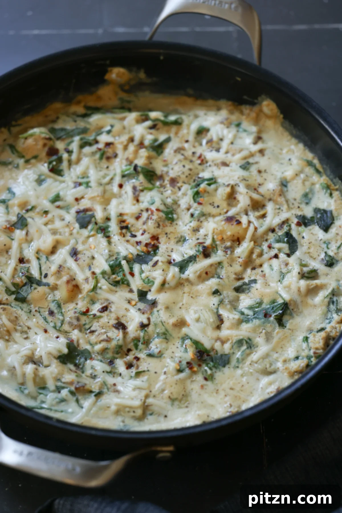 Delicious creamy spinach artichoke gnocchi served hot in a pan, ready to eat.