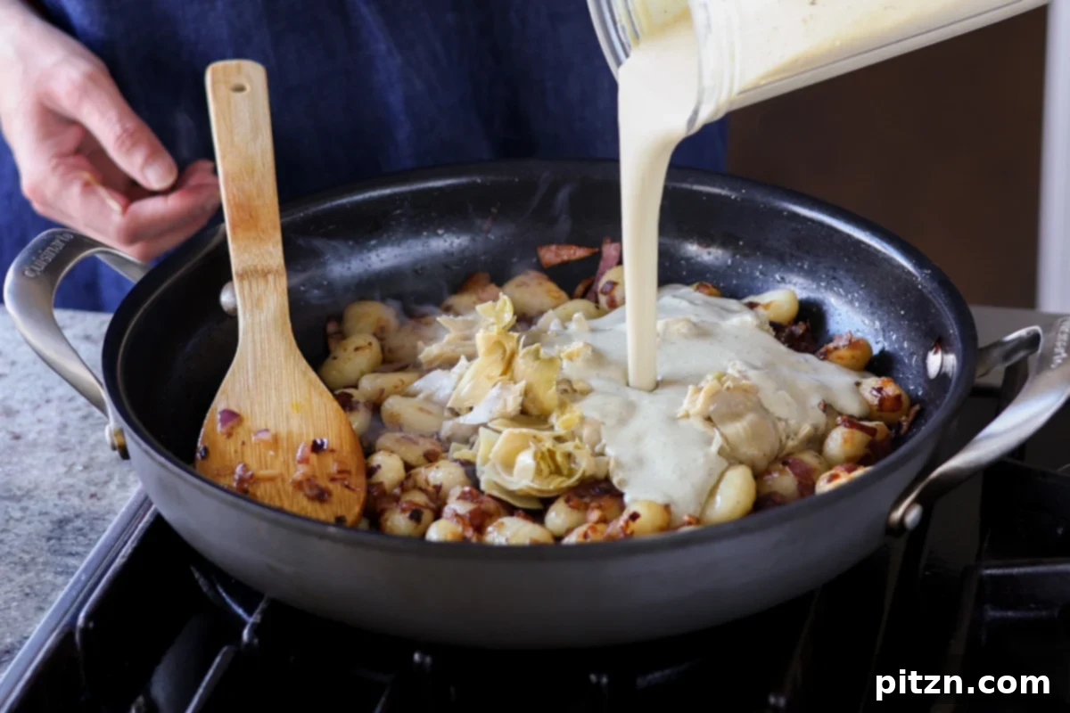 Pouring the creamy blender sauce into the pan with gnocchi and artichokes.