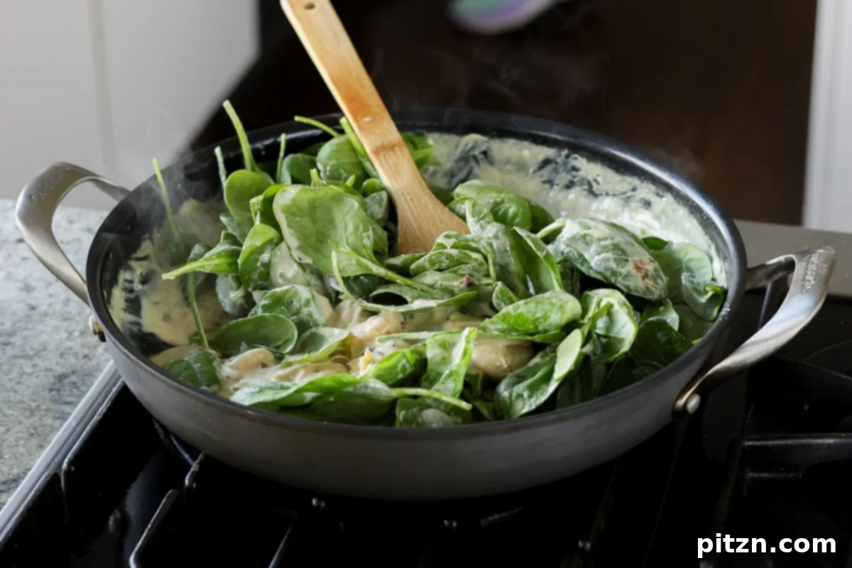 Adding fresh baby spinach to the creamy gnocchi sauce in the pan.