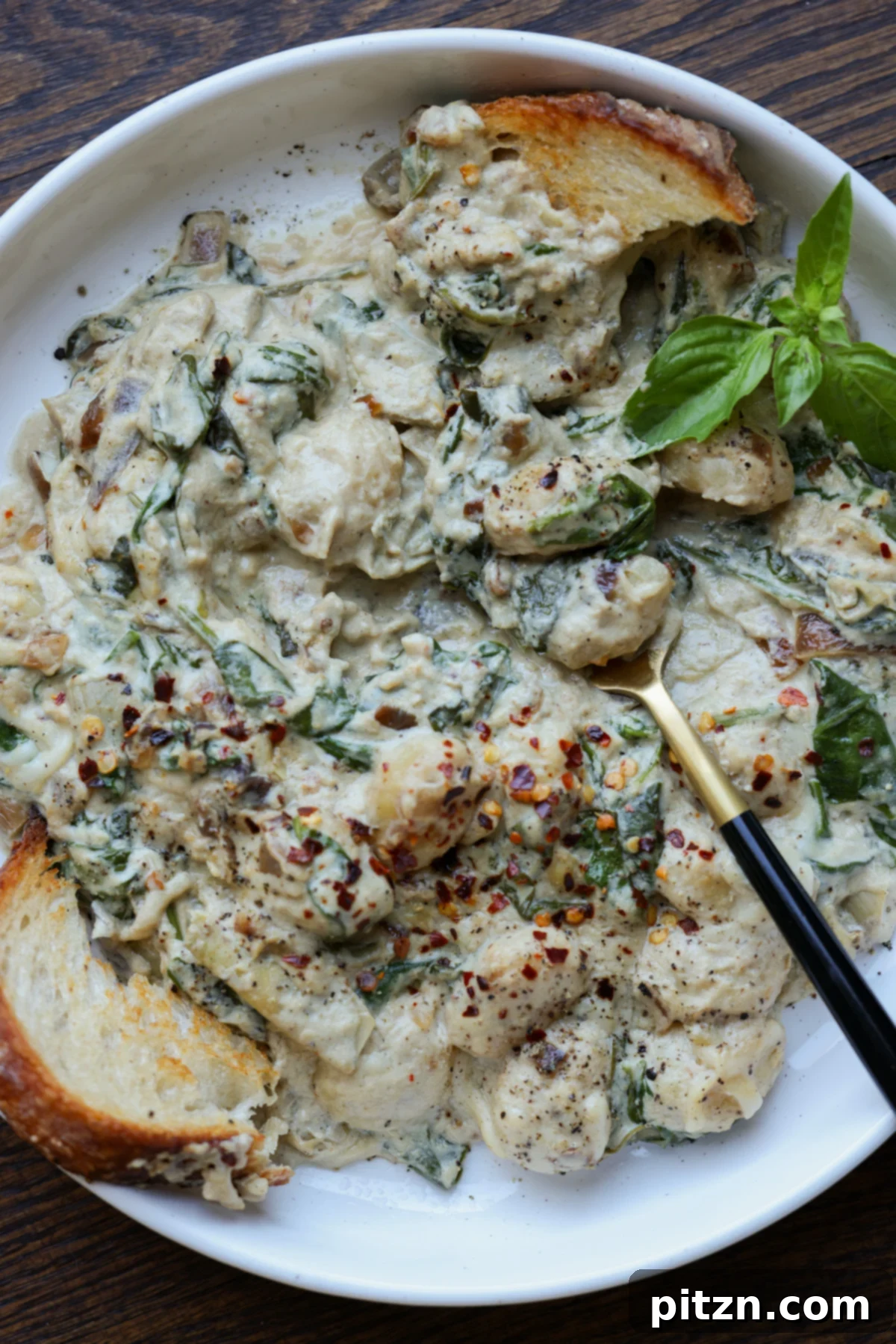 Close-up of a bowl filled with creamy spinach artichoke gnocchi, garnished with fresh basil.