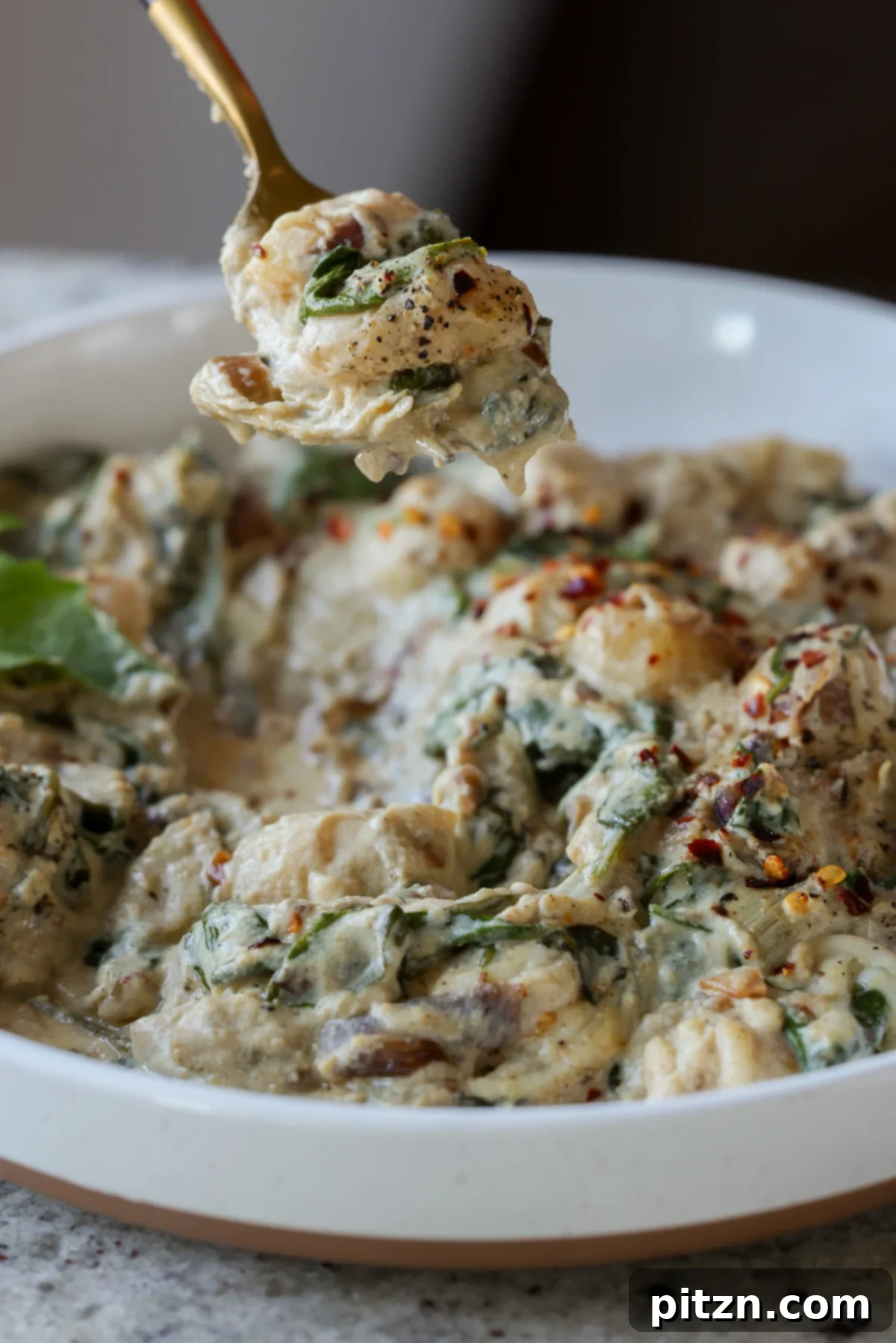 A fork taking a bite of spinach artichoke gnocchi, highlighting its creamy texture.