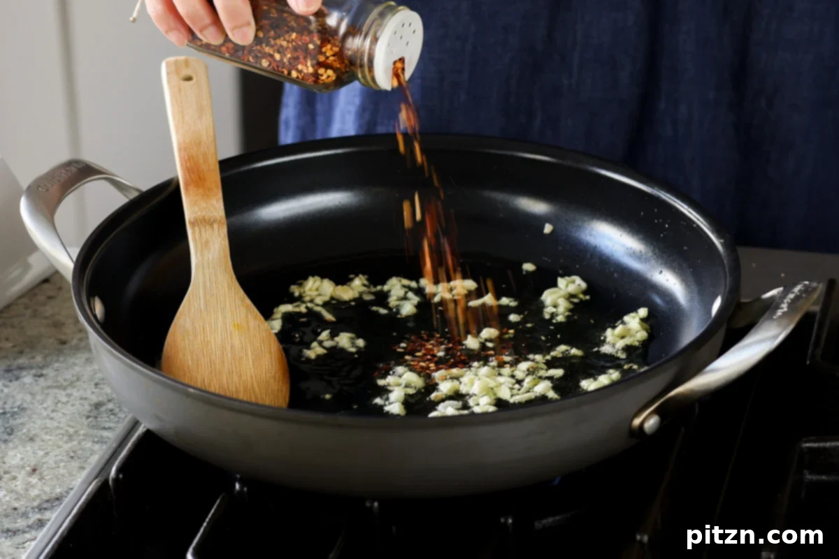 Adding crushed red pepper flakes to sautéed garlic in a pan.