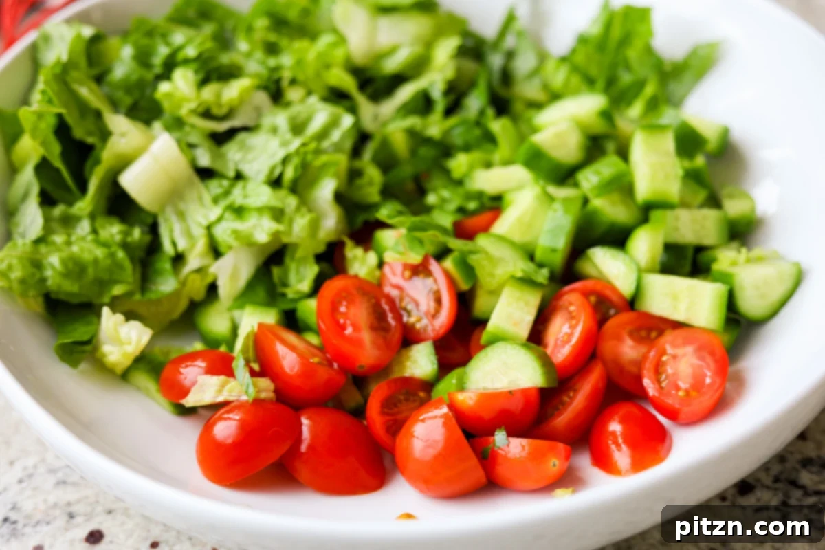 Sun-Drenched Spinach Salad with Zesty Olive-Chickpea Crunch 10 Freshly chopped vegetables, including greens, cucumber, and tomatoes, neatly arranged in a salad bowl before mixing.