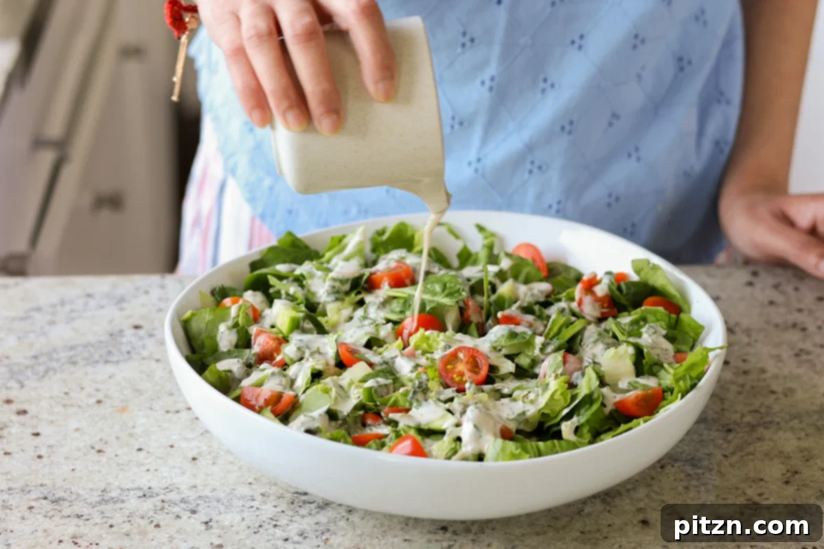 Sun-Drenched Spinach Salad with Zesty Olive-Chickpea Crunch 13 Creamy tahini dressing being generously poured over a bowl of fresh spinach salad, enhancing its appeal.