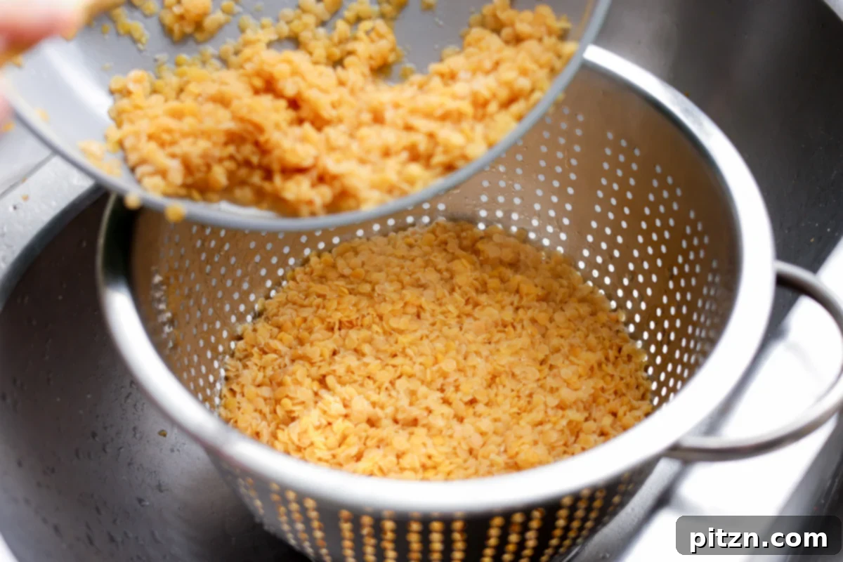 Lentil Protein World Tour Mix 13 Draining cooked lentils in a strainer, ensuring excess water is removed.
