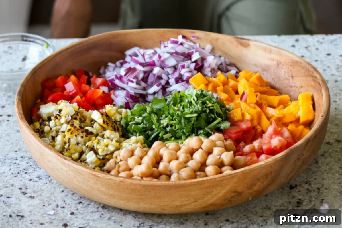 Tropical Chickpea & Mango Salad with Spiced Lime-Pepper Drizzle 14 A large bowl filled with all the prepped ingredients for Mango Chickpea Salad, including chickpeas, mango, corn, and other vegetables, before the dressing is added.