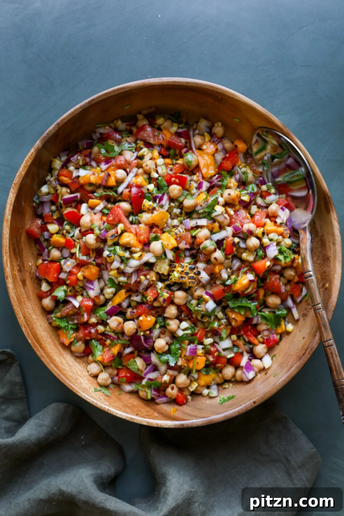 Tropical Chickpea & Mango Salad with Spiced Lime-Pepper Drizzle 17 A vibrant and colorful Mango Chickpea Salad served in a white bowl with a spoon, highlighting the freshness of the ingredients.