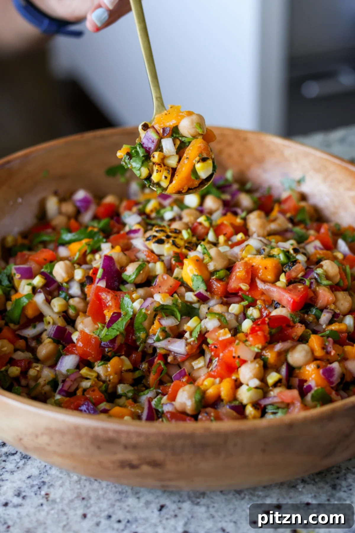 Tropical Chickpea & Mango Salad with Spiced Lime-Pepper Drizzle 3 A spoon scooping a generous portion of Mango Chickpea Salad from a bowl, showcasing the colorful blend of mango, chickpeas, corn, and red bell pepper.