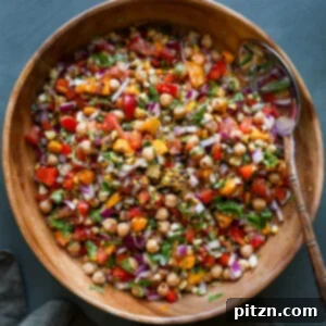 A serving bowl filled with Mango Chickpea Salad, showing a spoon resting in it, with vibrant colors of fruit and vegetables.