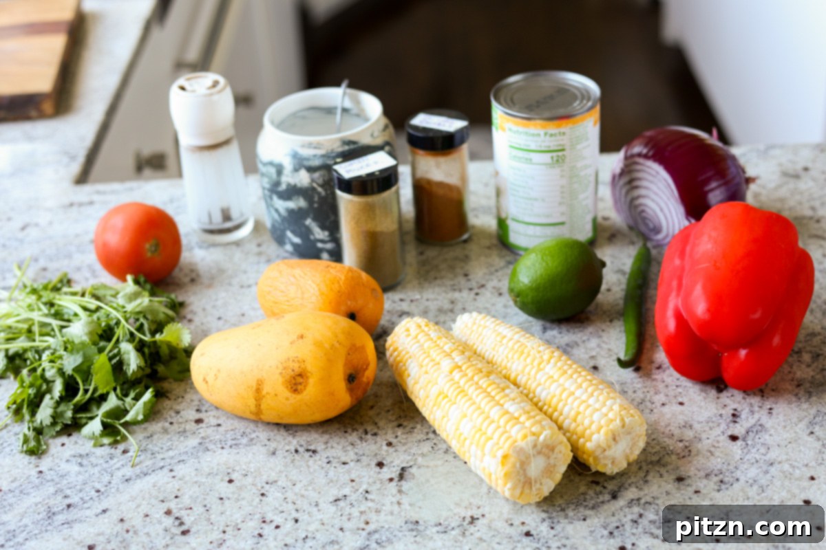 Tropical Chickpea & Mango Salad with Spiced Lime-Pepper Drizzle 6 Individual ingredients for Mango Chickpea Salad laid out on a surface, including chickpeas, corn on the cob, red bell pepper, mango, onion, and cilantro.