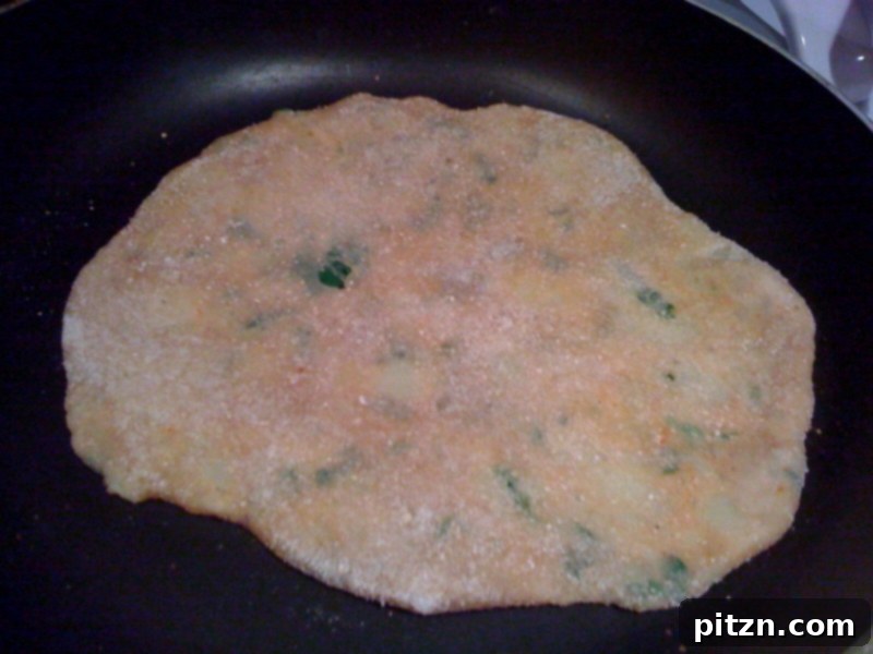 Mom's Aloo Paratha and Sanjeev Kapoor's Baghare Baingan A Flavorful Pairing 6 An Aloo Paratha cooking on a hot Tawa (Indian flat pan), showing the initial stages of frying.