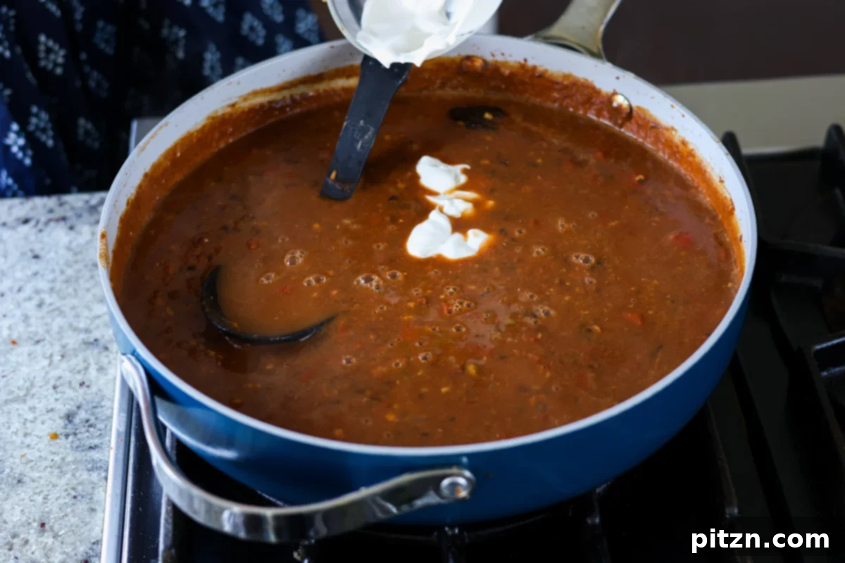 Restaurant-Quality Dal Makhani at Home 15 Non-dairy yogurt or cream being stirred into the simmering Dal Makhani for a creamy finish.