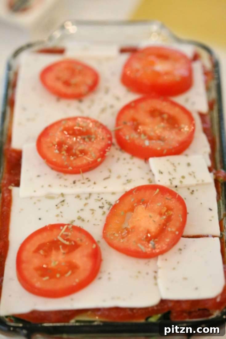 Cozy Vegan Veggie Lasagna for Two 8 The final top layer of lasagna featuring noodles, more sauce, cheese slices, fresh tomato slices, and a sprinkle of aromatic herbs before baking.