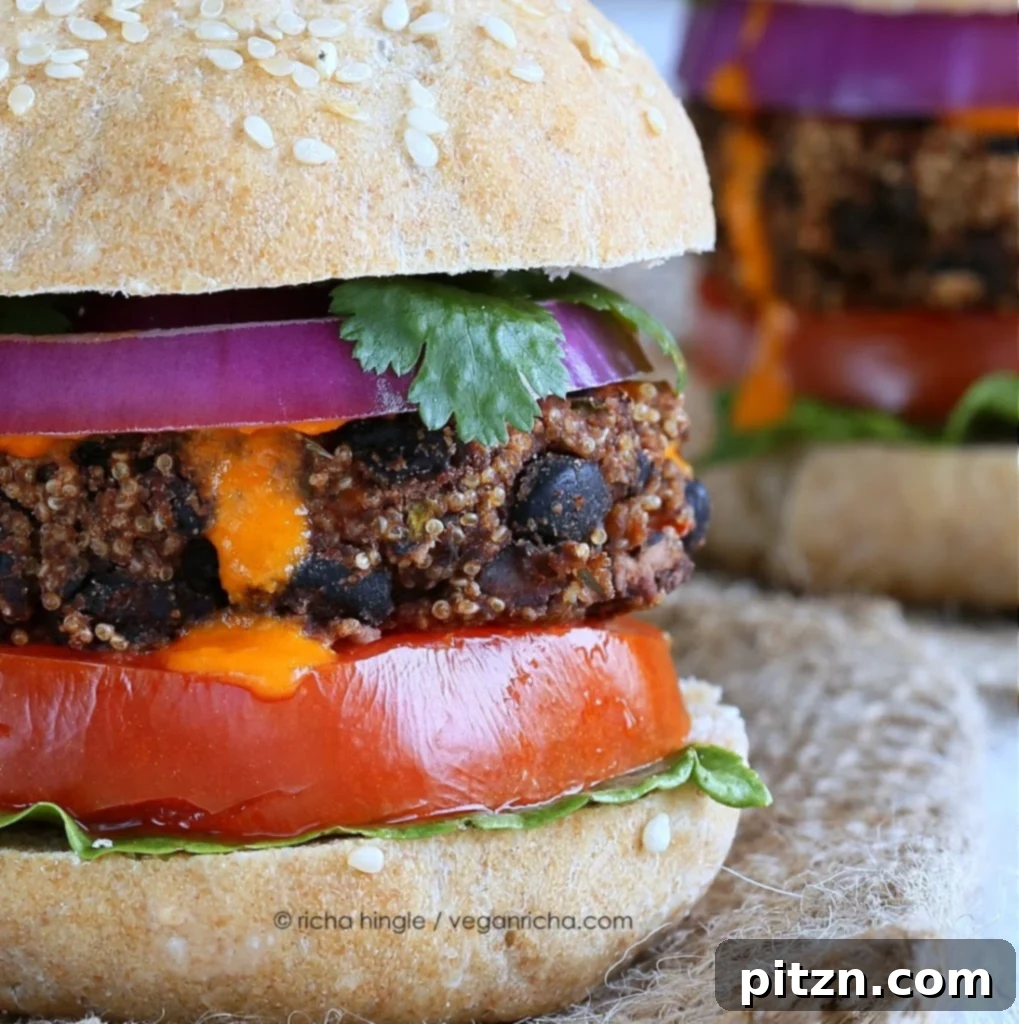 Two smoky Amaranth Black Bean Burgers stacked on a bun with fresh toppings