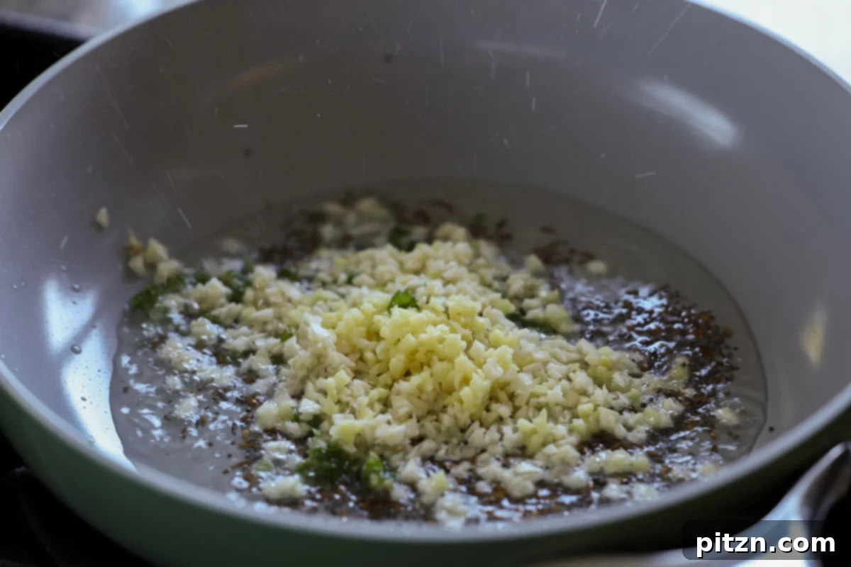 Adding chopped garlic to the sautéing aromatics in the pan