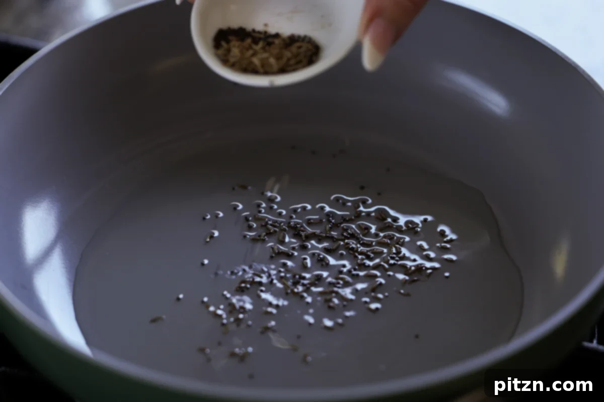 Adding whole spices (cumin and mustard seeds) to hot oil in a pan