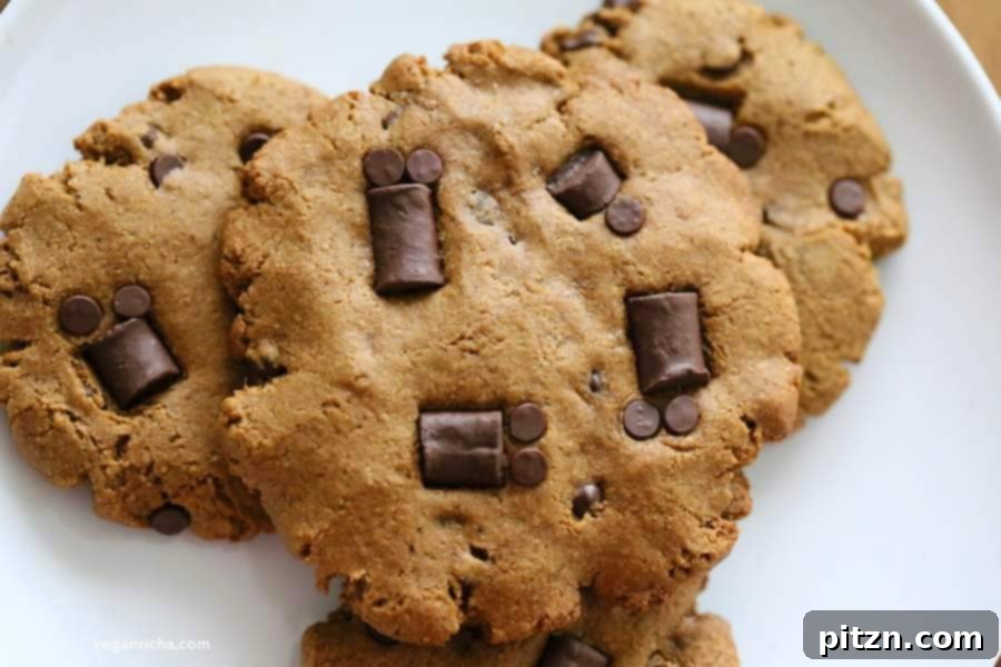 A selection of vegan pumpkin chocolate chip cookies, some decorated as spiders, on a rustic wooden surface.