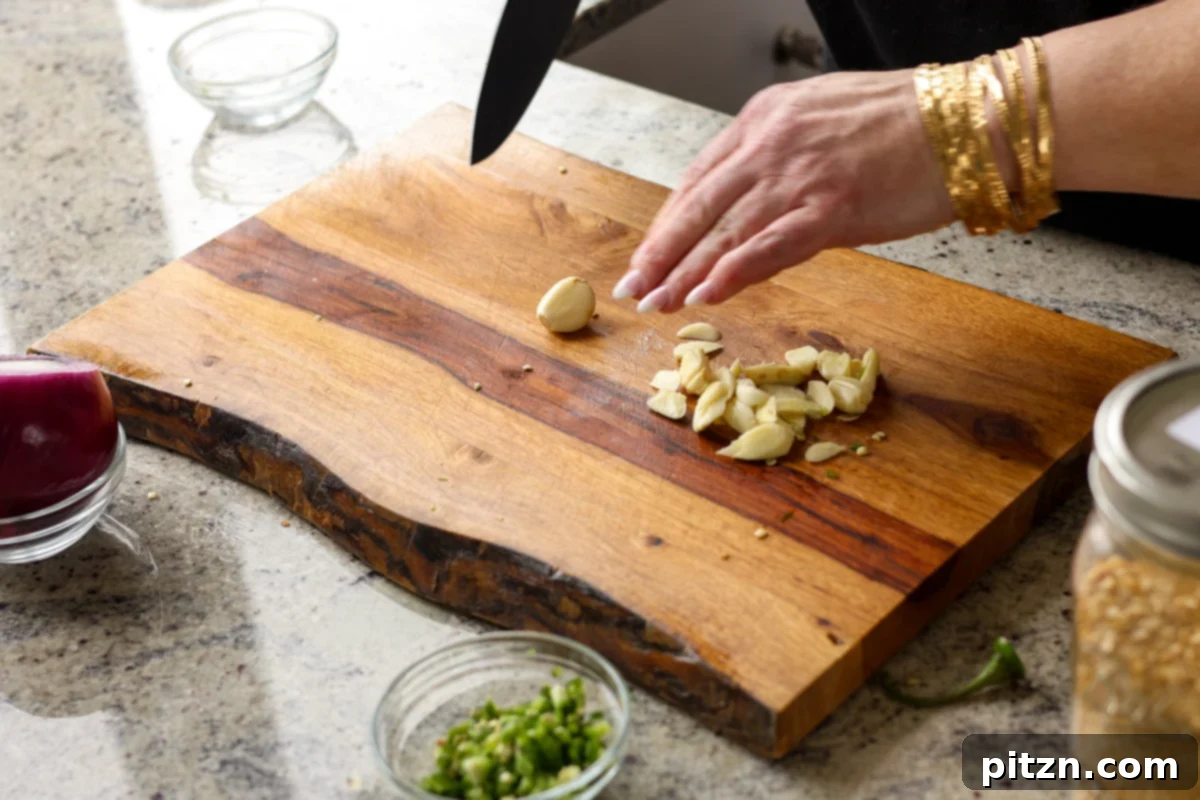 Dal Tadka Lentil Soup Mix in a Jar 12 Finely chopping fresh garlic cloves on a wooden cutting board.