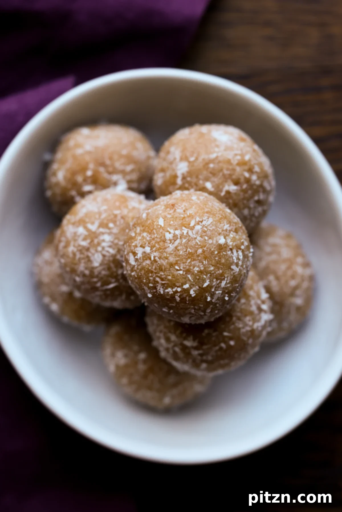 Toasted Cardamom Coconut Ladoo 3 A close-up view of three perfectly round toasted coconut ladoos resting on a pristine white serving plate, highlighting their golden texture.