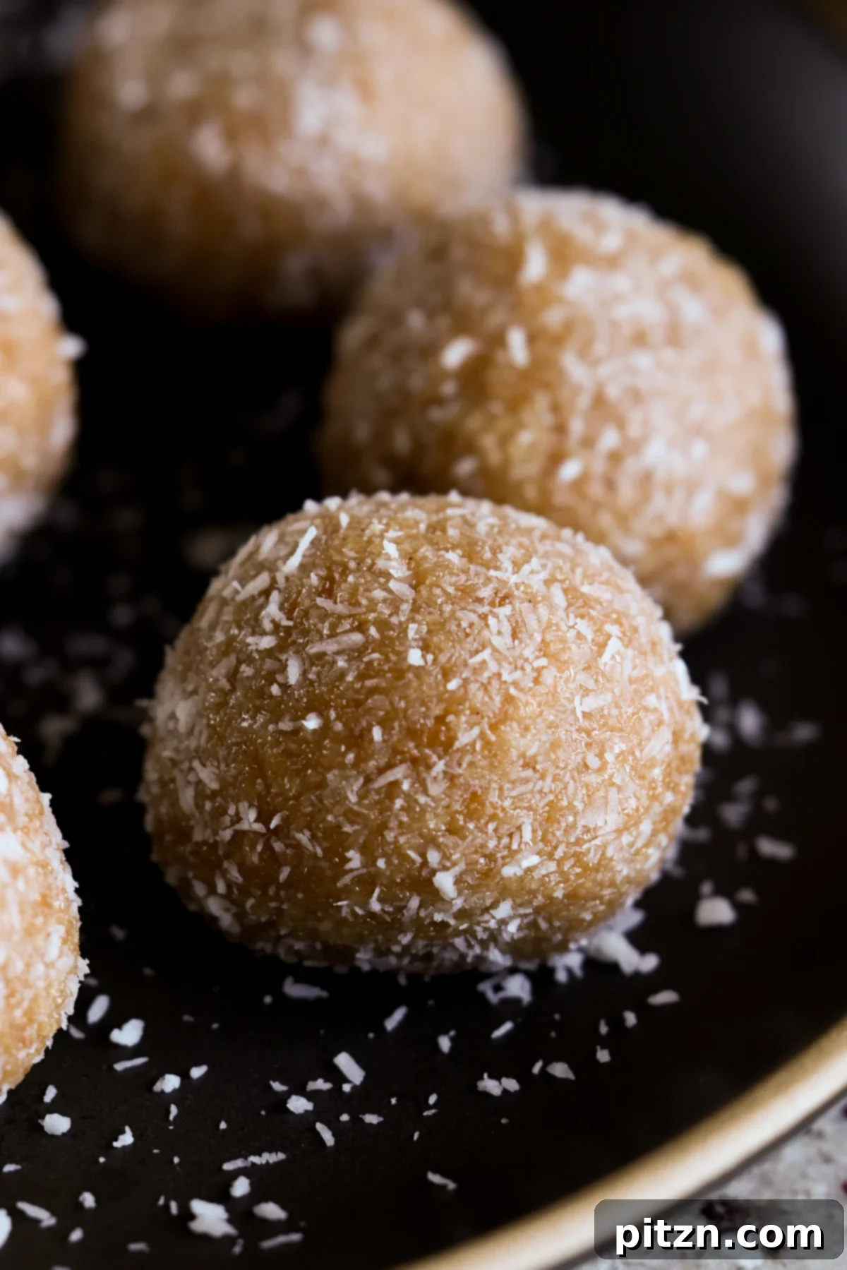 Toasted Cardamom Coconut Ladoo 4 Three toasted coconut ladoos arranged on a stylish black plate, with a focus on their slightly browned exterior and inviting texture.
