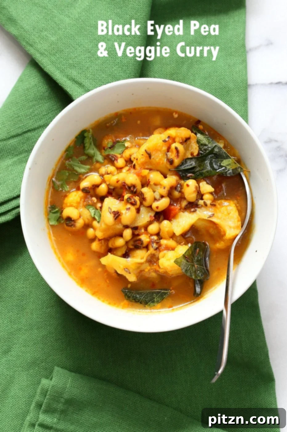Coconutty Black Eyed Pea Curry with Cauliflower and Potatoes in a white bowl, garnished with fresh herbs, alongside a green napkin. A hearty, delicious, and easy Instant Pot recipe. Vegan, Gluten-free, Soy-free, Nut-free.