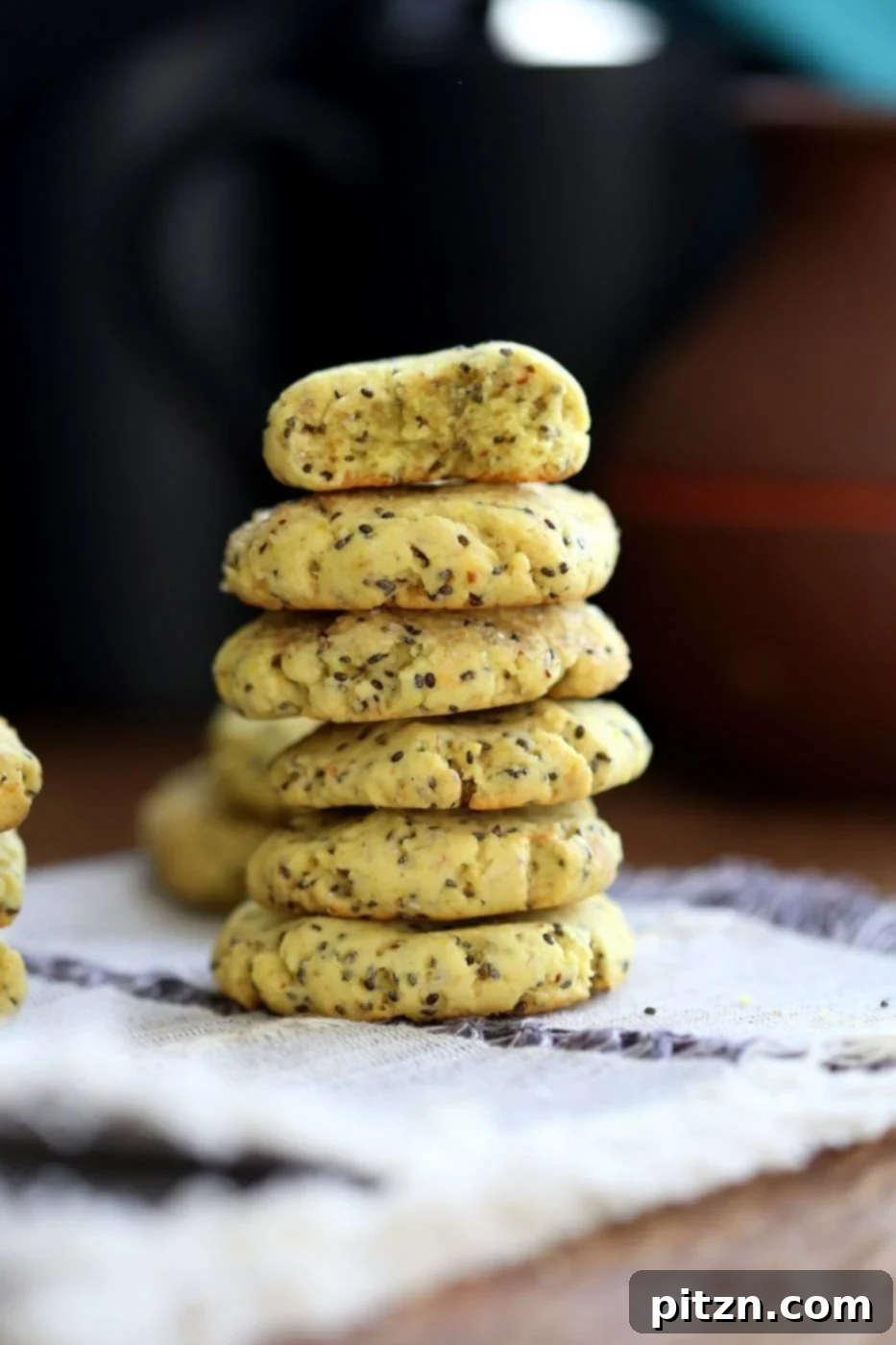 Perfectly stacked vegan lemon cookies resting on a grey napkin atop a rustic wooden table, showcasing their soft, zesty appeal.