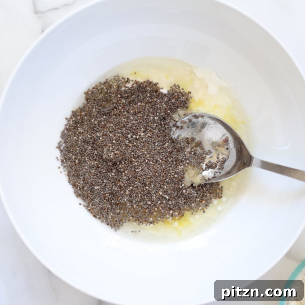 Close-up of wet ingredients including lemon zest, lemon juice, non-dairy yogurt, and chia seeds in a white bowl, ready for vegan lemon cookie preparation.