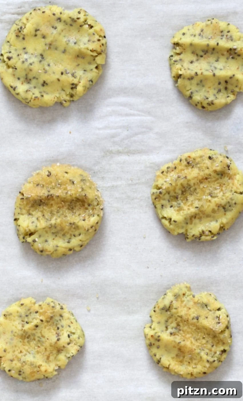 Unbaked vegan lemon cookie dough balls, lightly flattened and ready for the oven on a parchment-lined baking sheet.