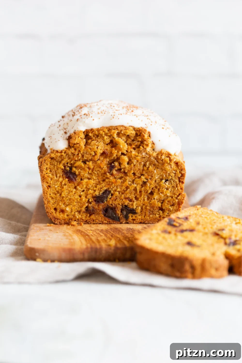 Side view of a loaf of vegan pumpkin carrot bread with dairy-free icing, showcasing its moist texture.