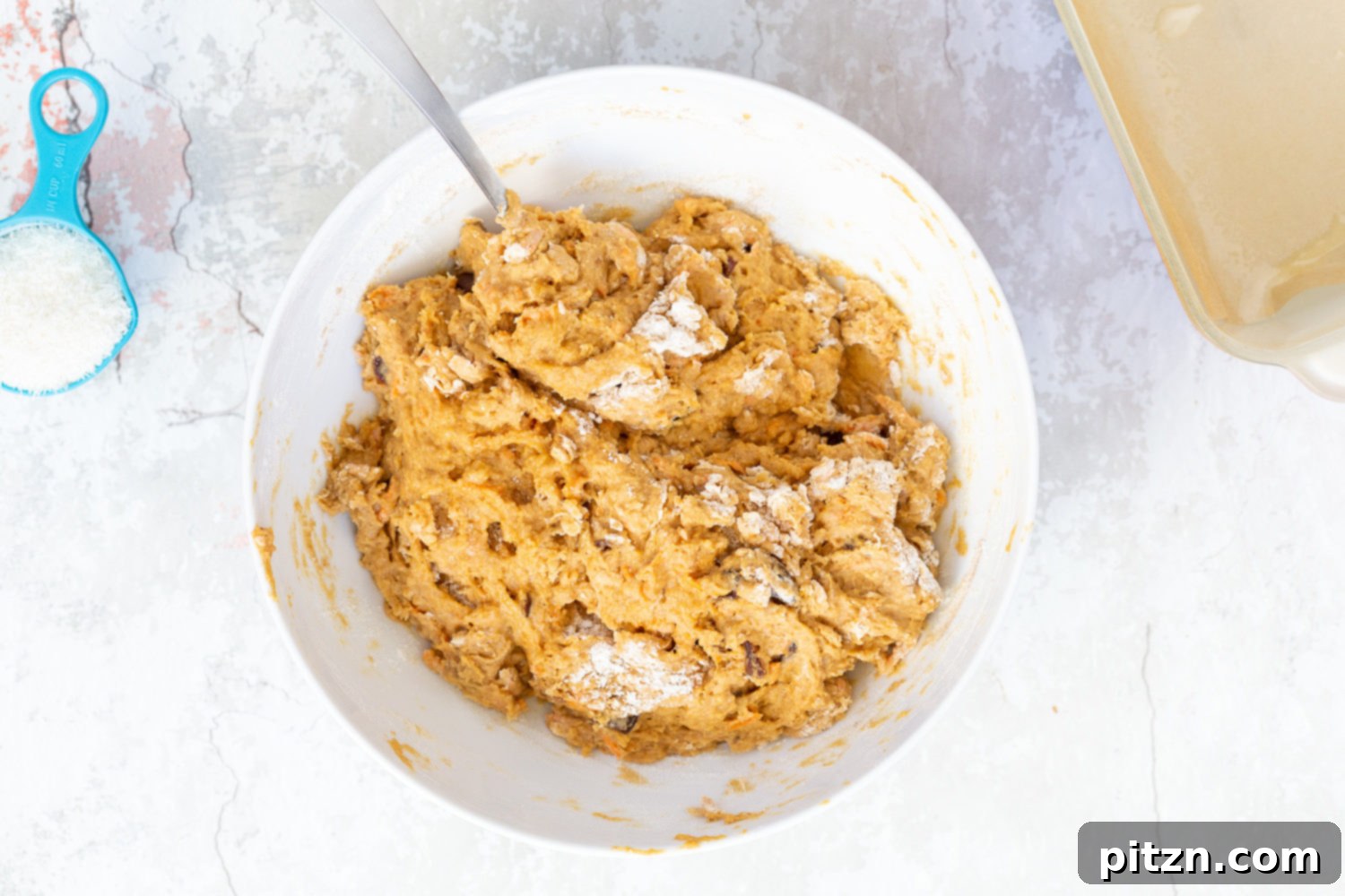 More flour being added to pumpkin bread batter to make it thicker, illustrating the consistency adjustment.