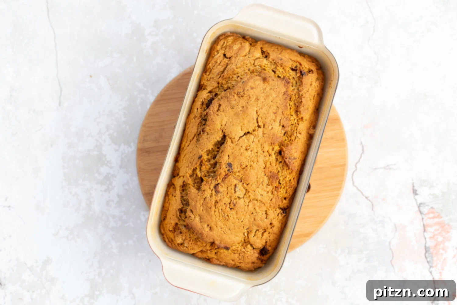 A freshly baked loaf of vegan pumpkin carrot bread cooling on a chopping board after being removed from the oven.