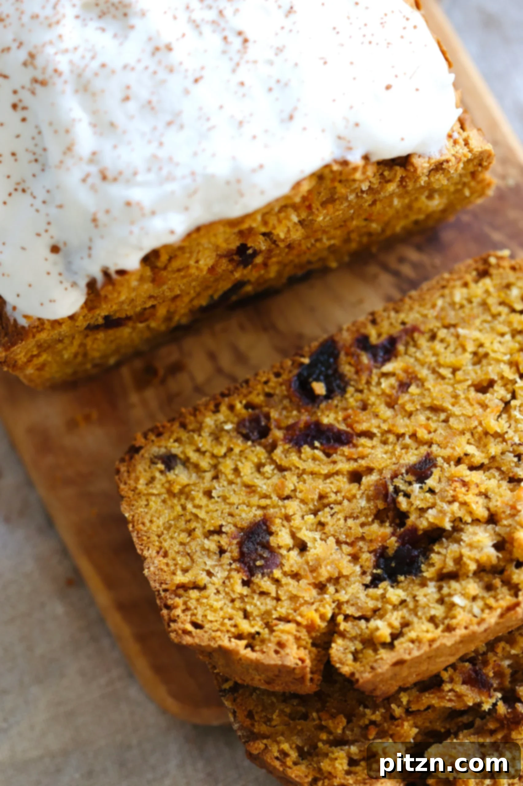 A sliced loaf of vegan pumpkin carrot bread on a wooden cutting board, revealing the tender crumb and carrot flecks.