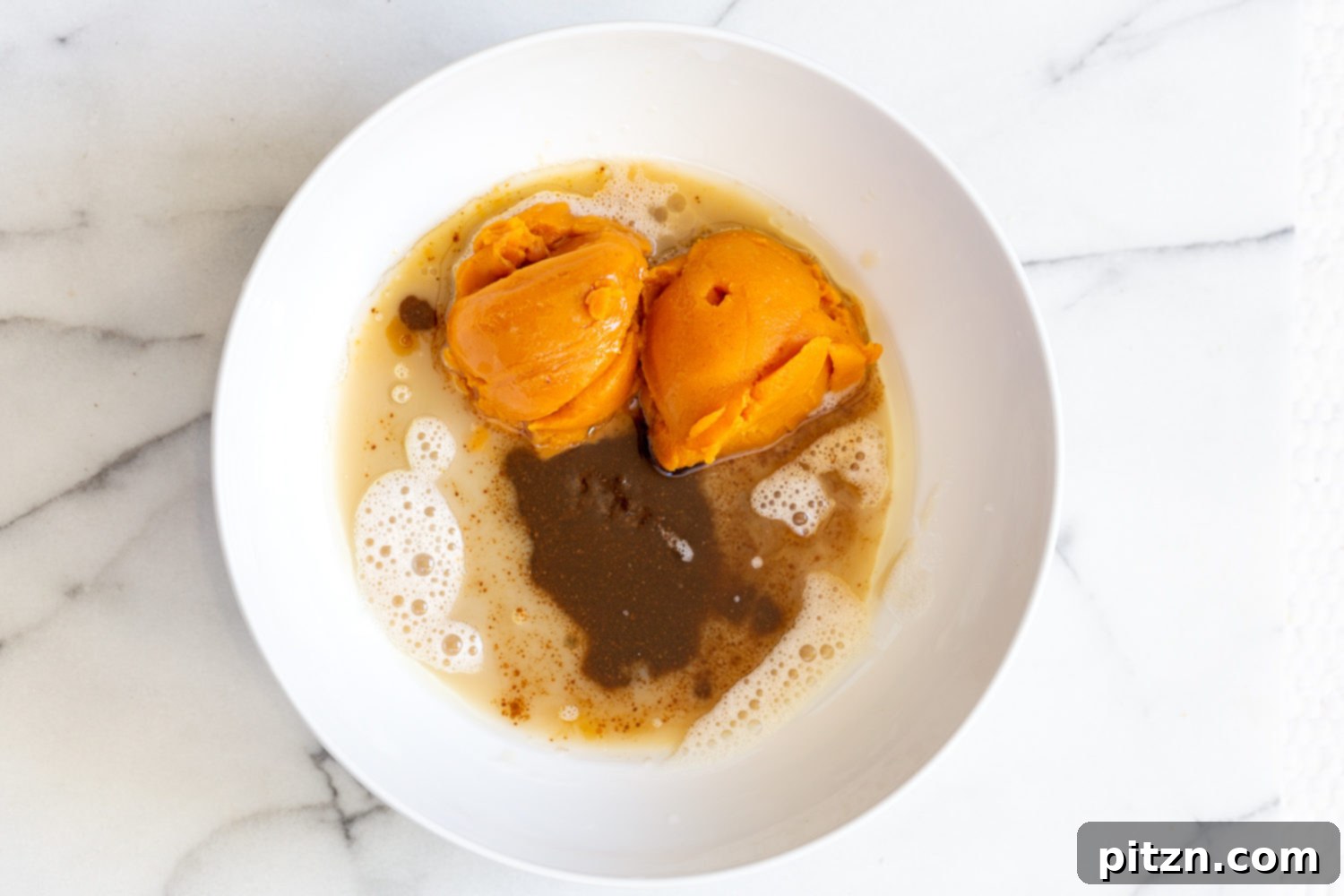 Wet ingredients for vegan pumpkin bread, including pumpkin puree and oil, mixed in a white bowl.