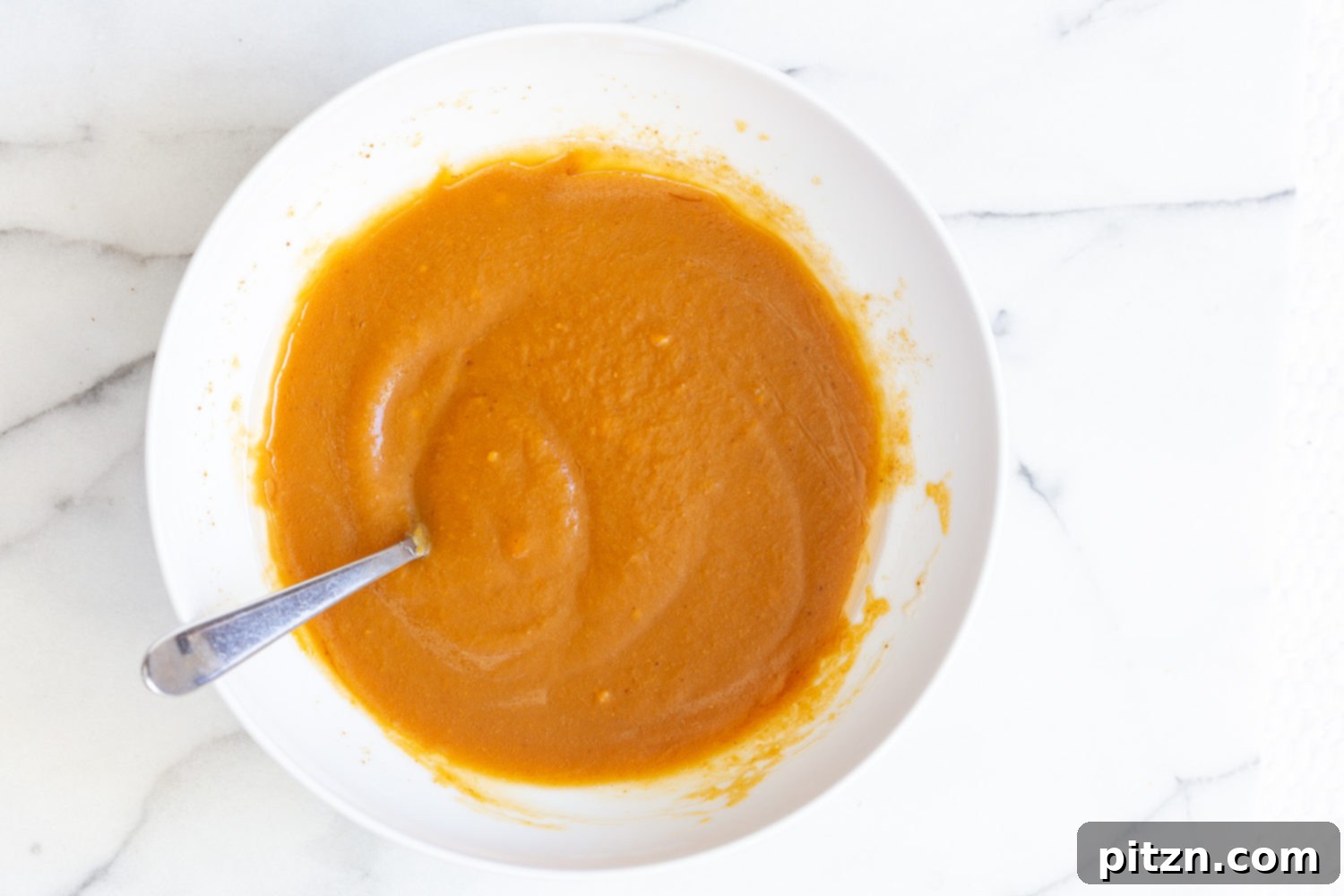 Vegan pumpkin carrot bread batter being stirred in a bowl, showing initial mixing of wet ingredients.