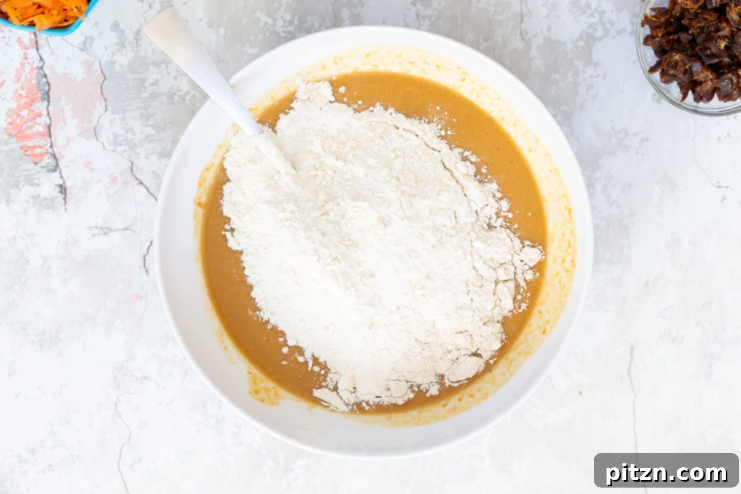Flour being added to vegan carrot pumpkin bread batter, showing the dry ingredients joining the wet.