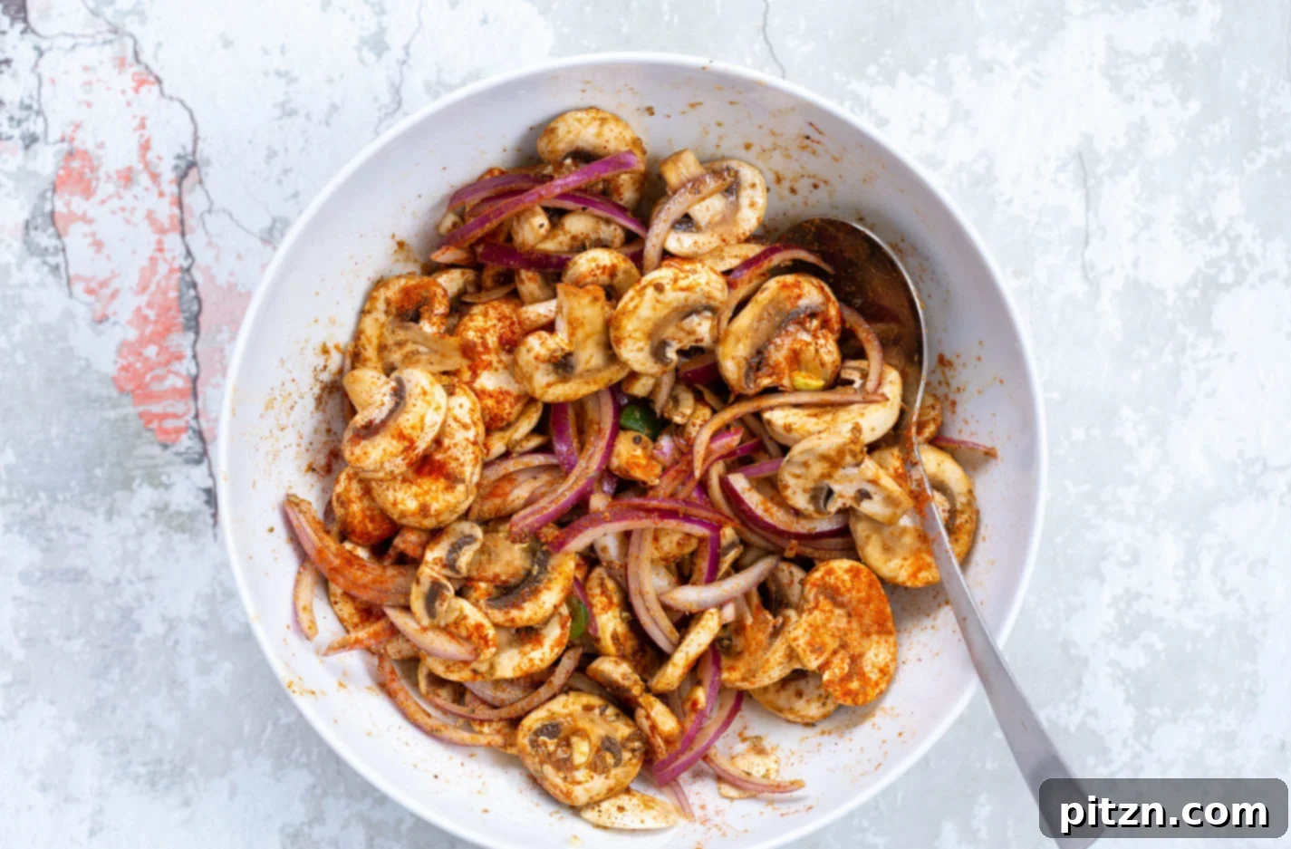 Sliced mushrooms and onions coated in a vibrant, aromatic spice blend within a white mixing bowl, showcasing the marinading stage for Vegan Carnitas.