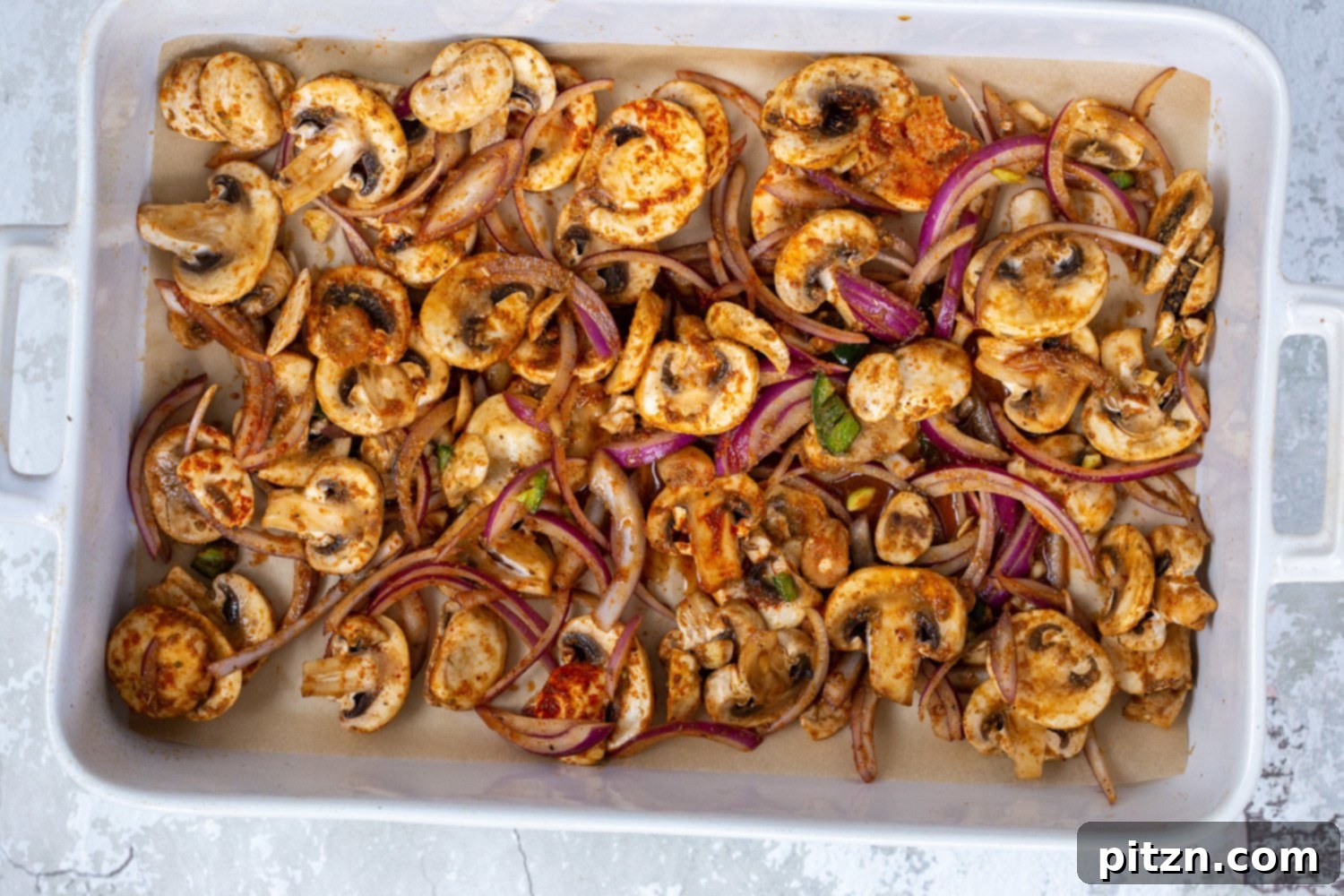 Marinated mushroom and onion mixture spread evenly in a white baking dish lined with parchment paper, prepared for baking into Vegan Carnitas.
