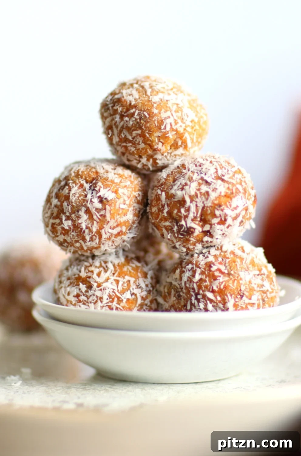 Delicious and healthy Vegan Carrot Cake Bites stacked on a rustic plate, garnished with shredded coconut and a hint of glaze. Perfect for a quick, wholesome snack.