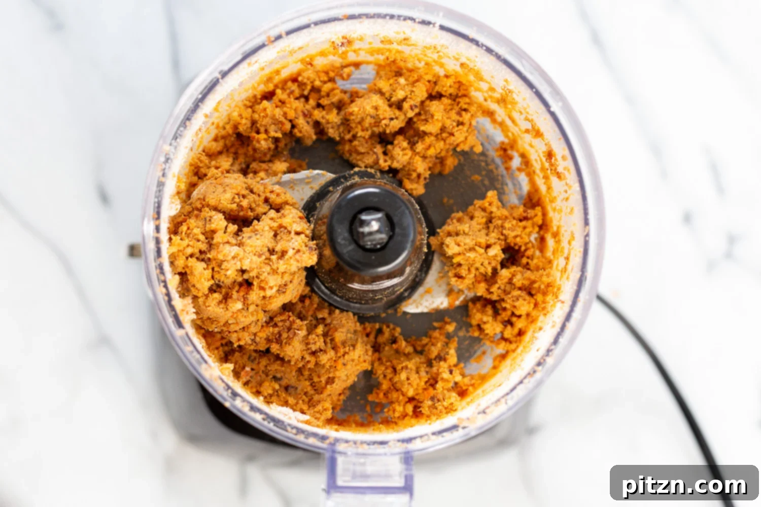 All the ingredients for Vegan Carrot Cake Bites being pulsed together in a food processor to form a cohesive dough.