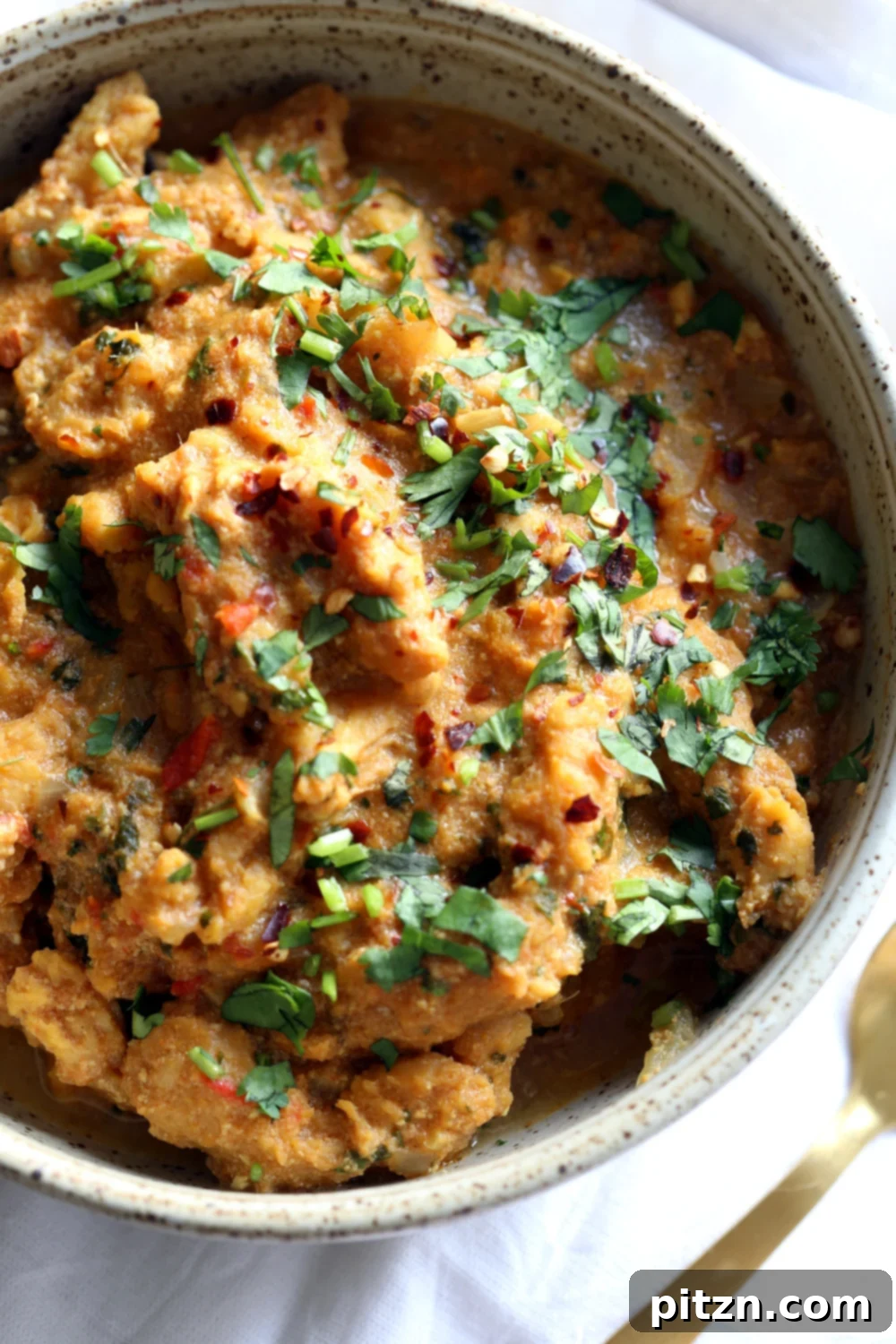 overhead shot of a bowl of vegan fenugreek chicken curry topped with chopped cilantro