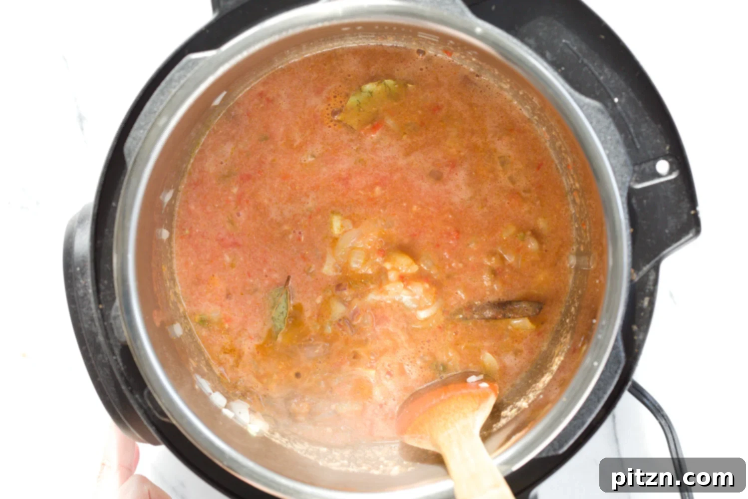 onions, garlic, tomato paste and spices being stirred in an Instant pot to make Vegan curry recipe