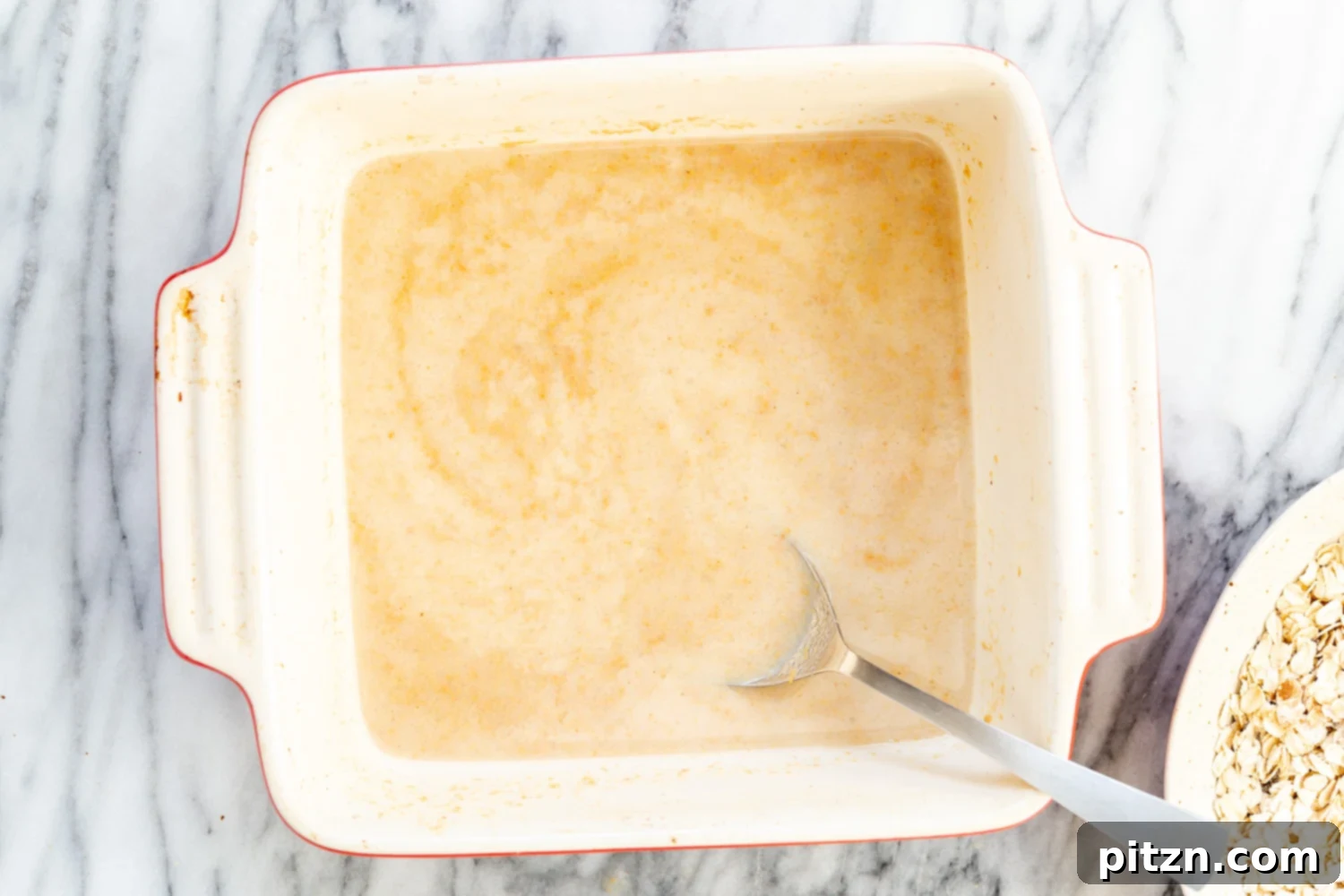 Mixing the wet and dry ingredients for Peanut Butter and Jelly Oatmeal in a white baking dish.