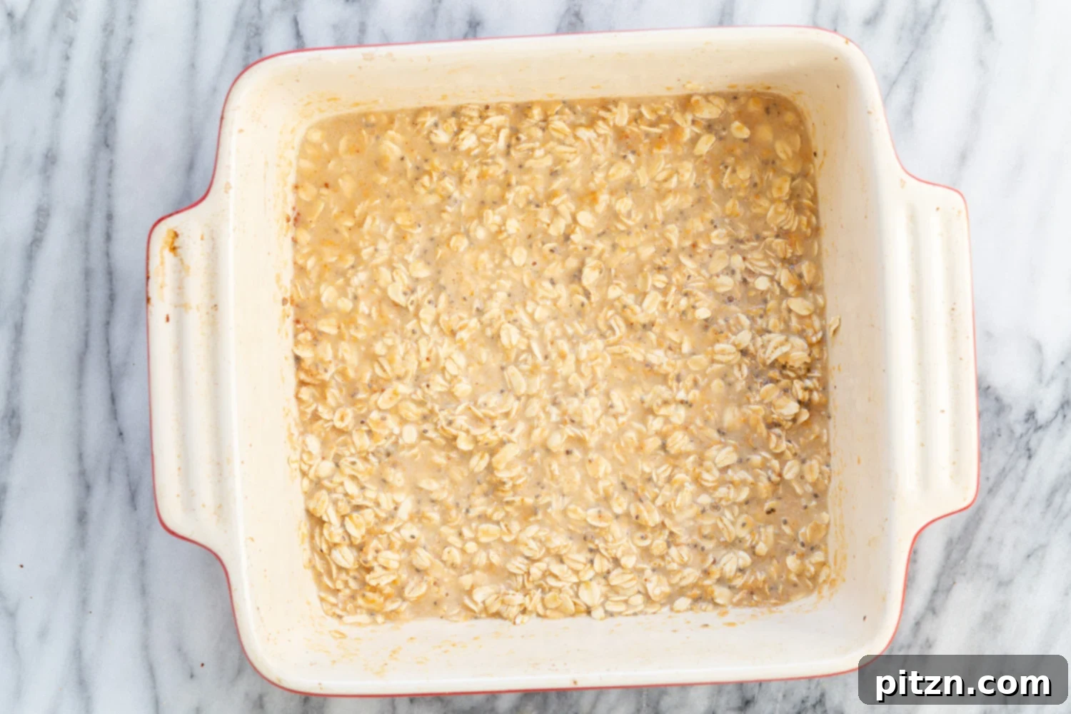 Peanut Butter and Jelly Oatmeal mixture in a white baking dish before baking, showing the berry swirls.
