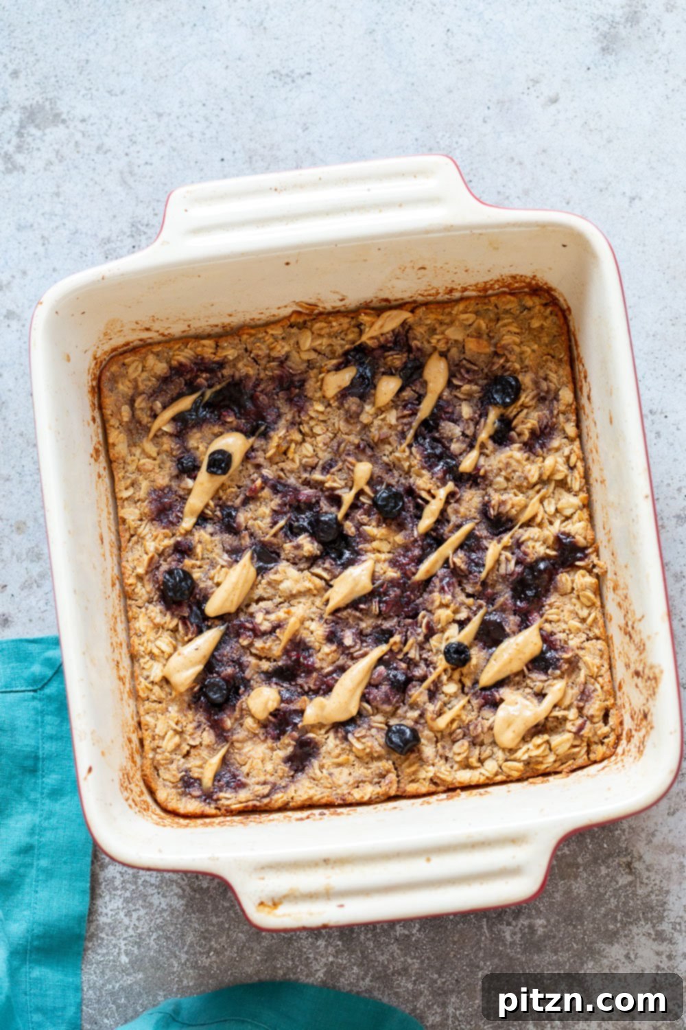 A slice of Vegan Peanut Butter and Jelly Baked Oatmeal on a white plate, garnished with fresh berries and a drizzle of peanut butter.