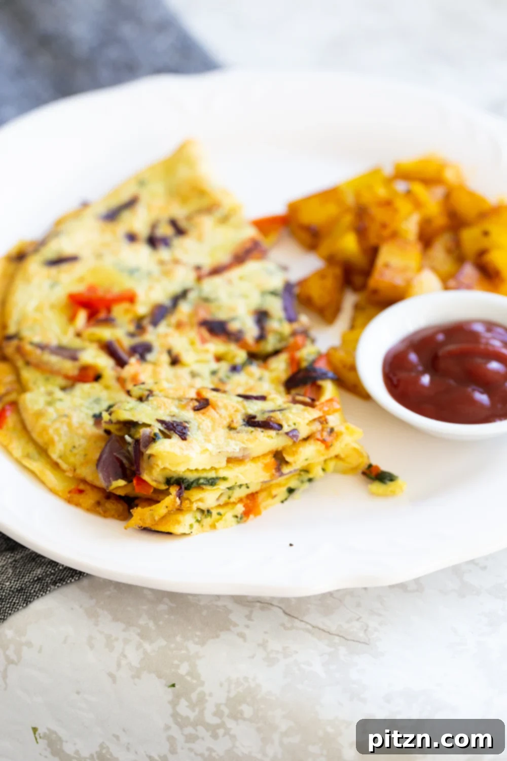 A vibrant, veggie-packed Vegan Omelet served on a white plate with breakfast potatoes and a dollop of ketchup
